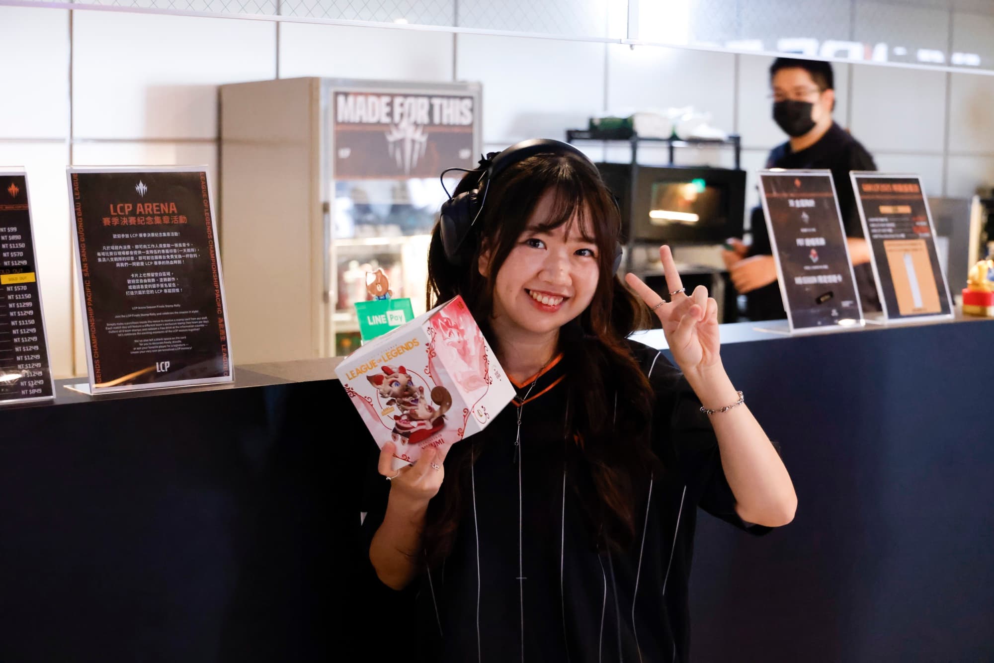 粉絲在 LCP Arena 大廳帶耳機拿 League of Legends 週邊比 YA