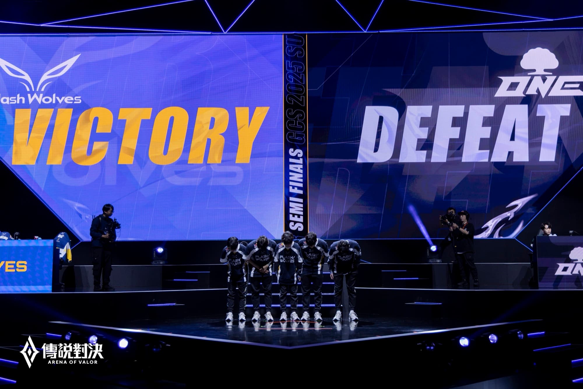 場館大螢幕左右各顯示 VICTORY 與 DEFEAT 賽果，台上人員並排站立