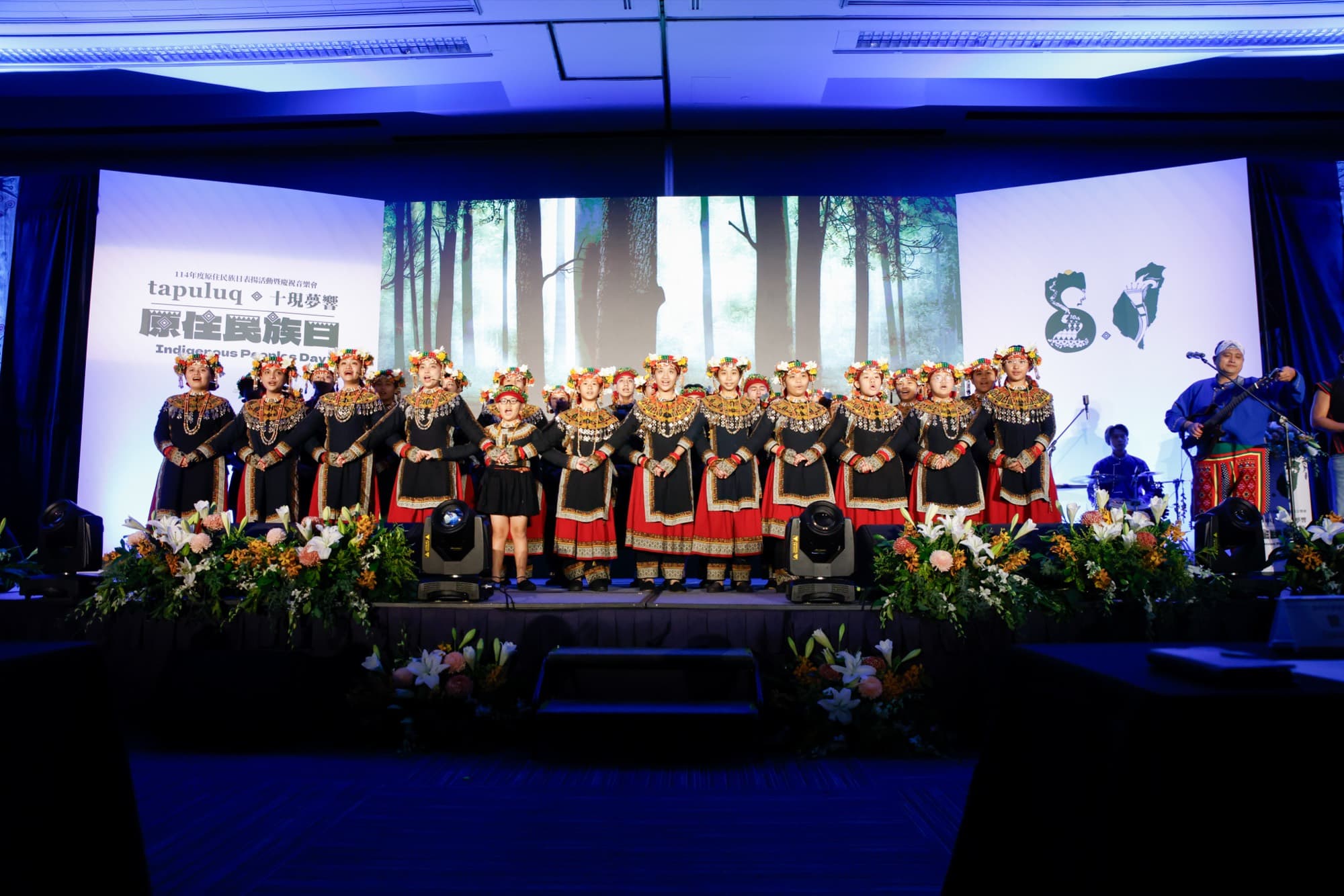 合唱團於主視覺背板前列隊演唱，前景花藝