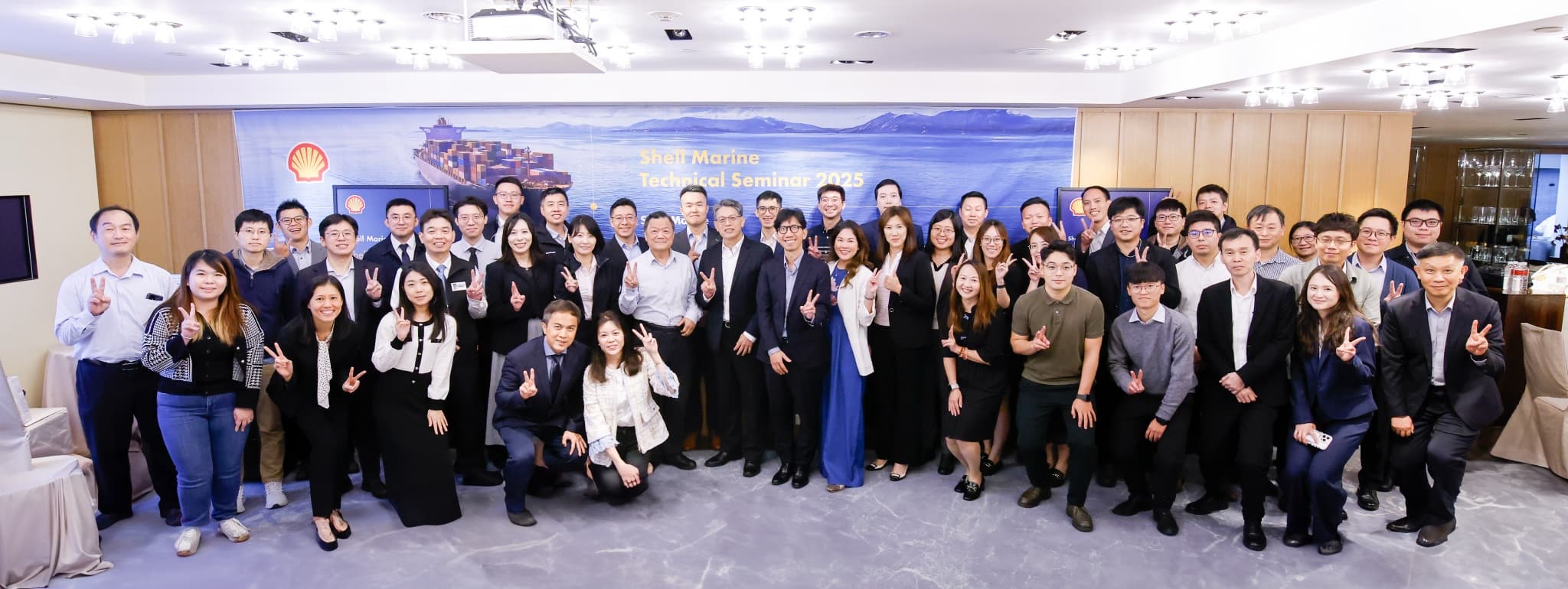 全體與會者約六十人在 Shell Marine Technical Seminar 2025 橫幅背板前合影，多數人比出勝利手勢