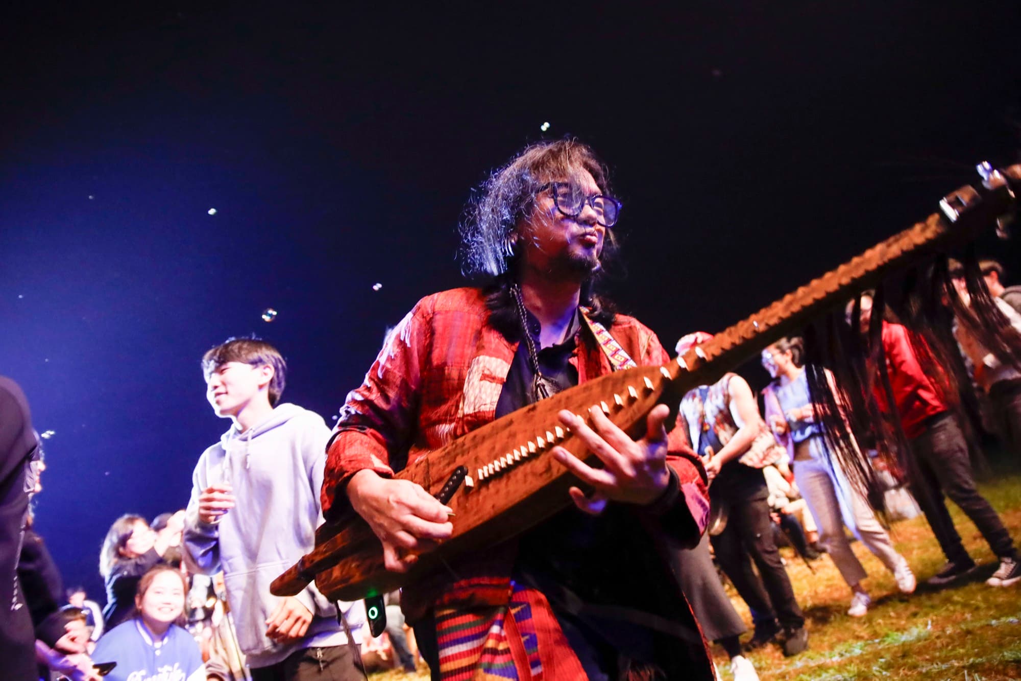 夜間人群中表演者手抱木製傳統撥弦樂器演奏