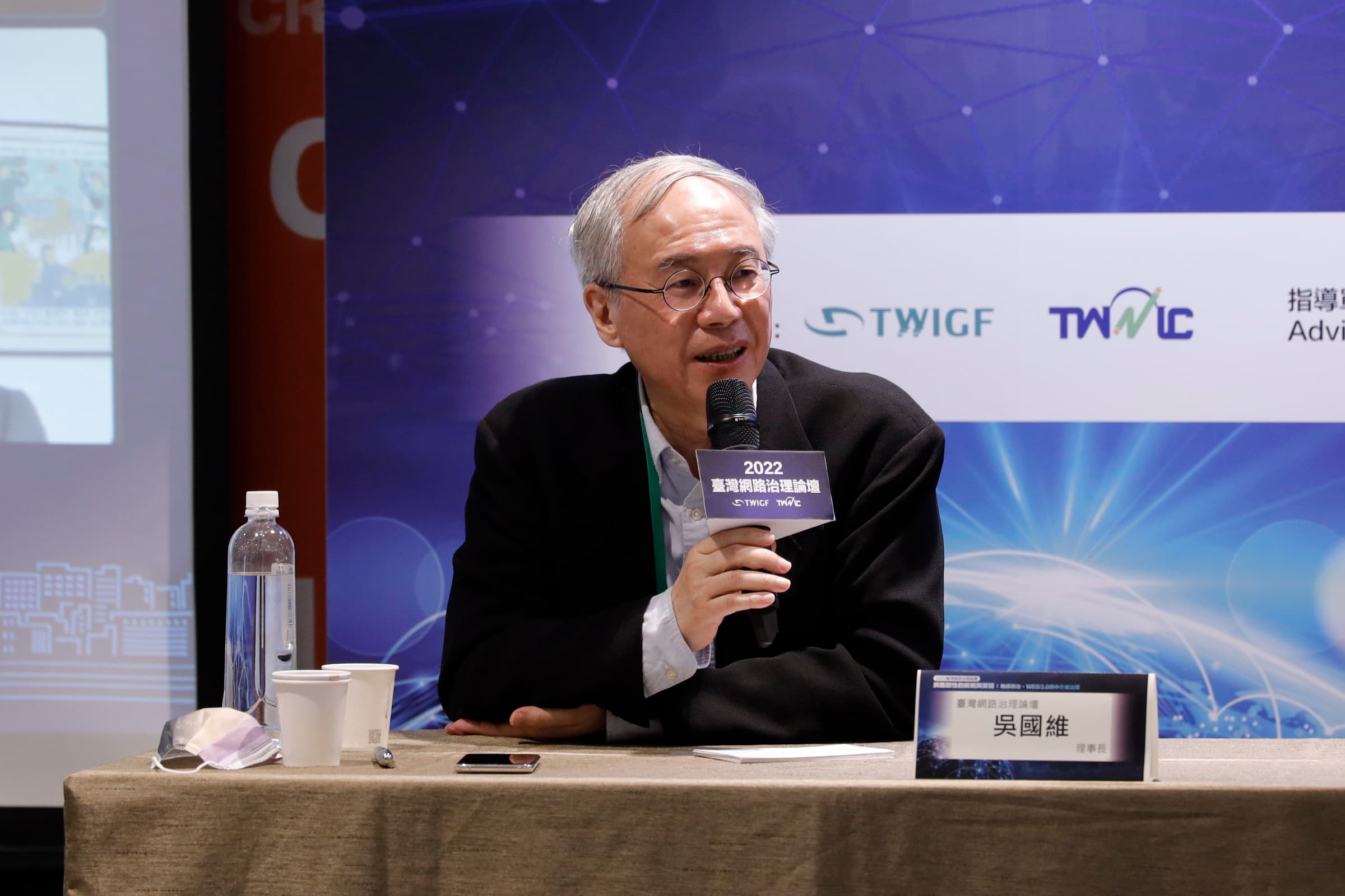 一位年長男性論壇代表於座談席手持麥克風發言，身後為 TWIGF、TWNIC 識別