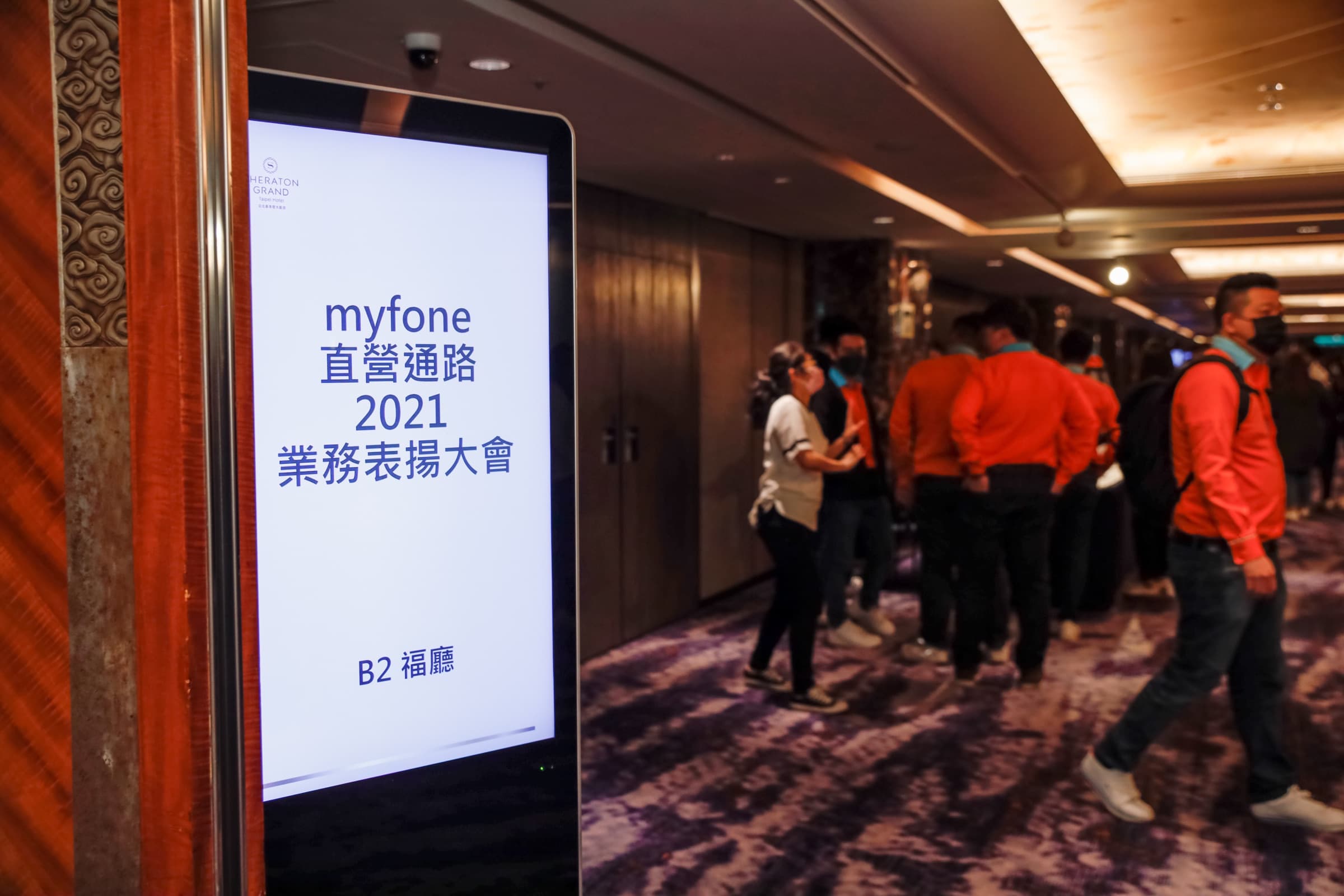 立式指示牌寫著『myfone 直營通路 2021 業務表揚大會・B2 福廳』，背景有走動的與會者