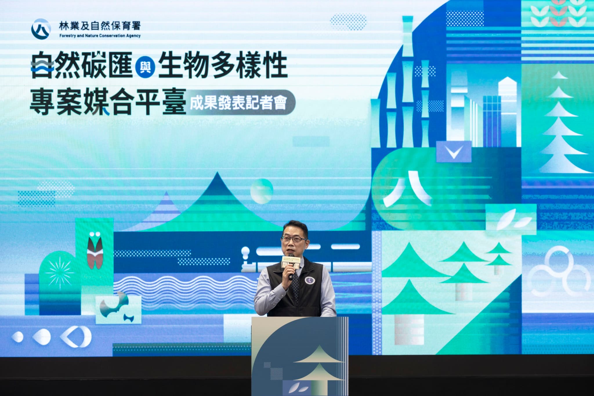 身穿林業及自然保育署背心的長官站在講台持麥克風致詞,背後 LED 大螢幕完整顯示記者會主視覺。