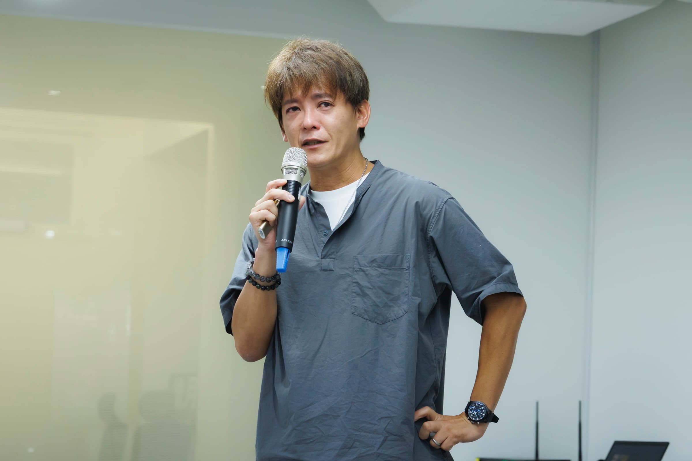 謝哲青手持麥克風、一手叉腰於淺色背景前演講,表情自然、臉部清晰