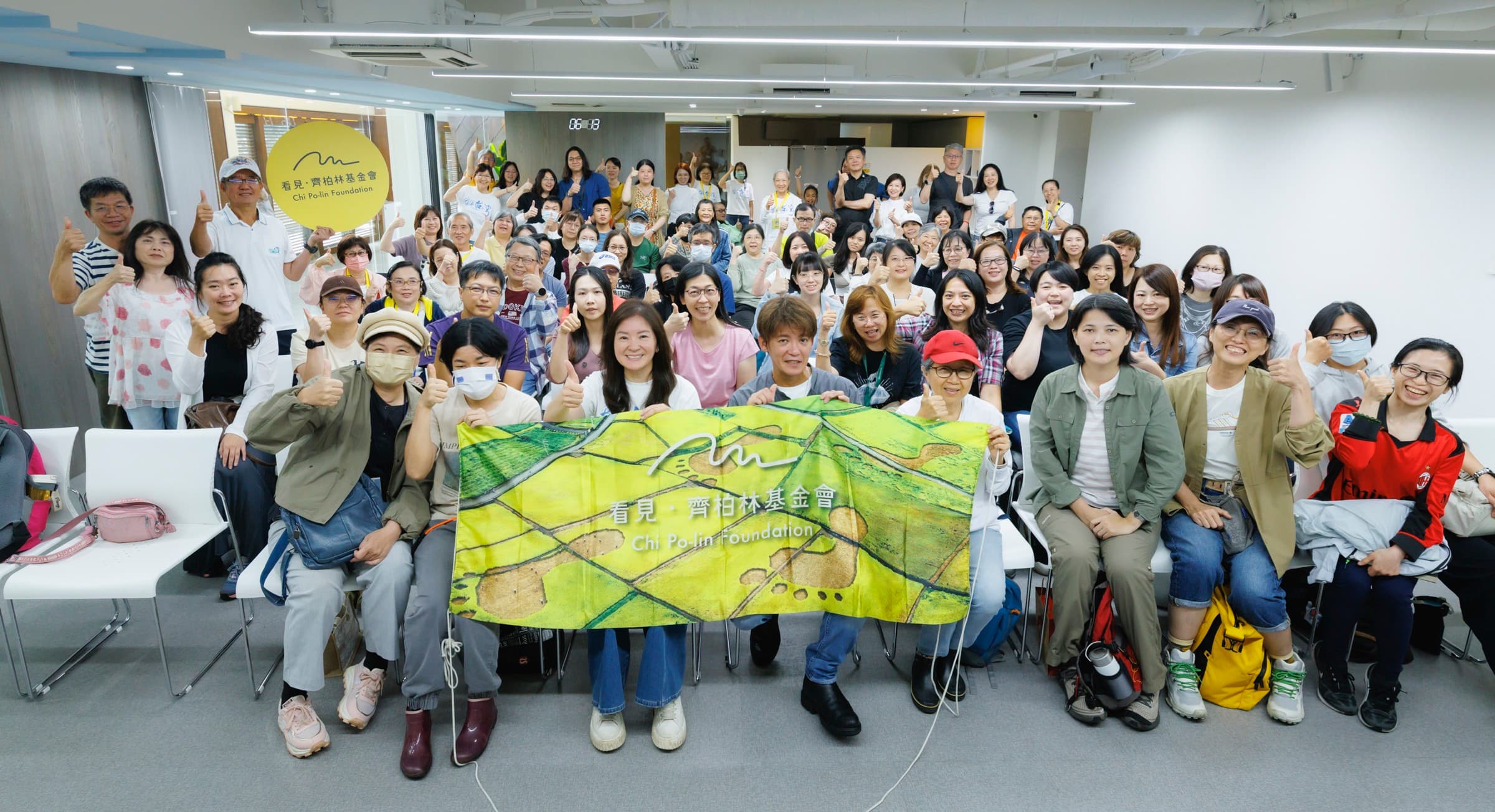 講堂內滿場聽眾比讚,謝哲青與主持人、基金會夥伴於前排共持印有空拍稻田的『看見・齊柏林基金會』布條,牆上有基金會 logo
