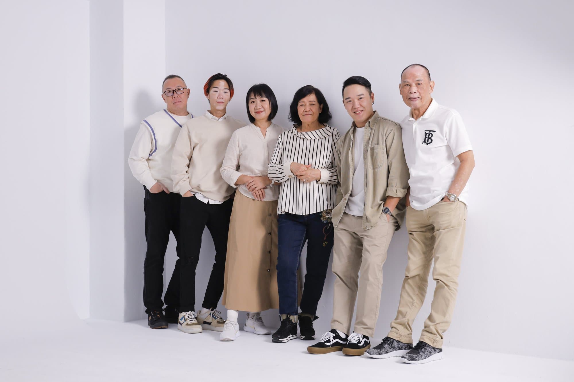 六位家人倚著白色牆面並排站立的全身群像
