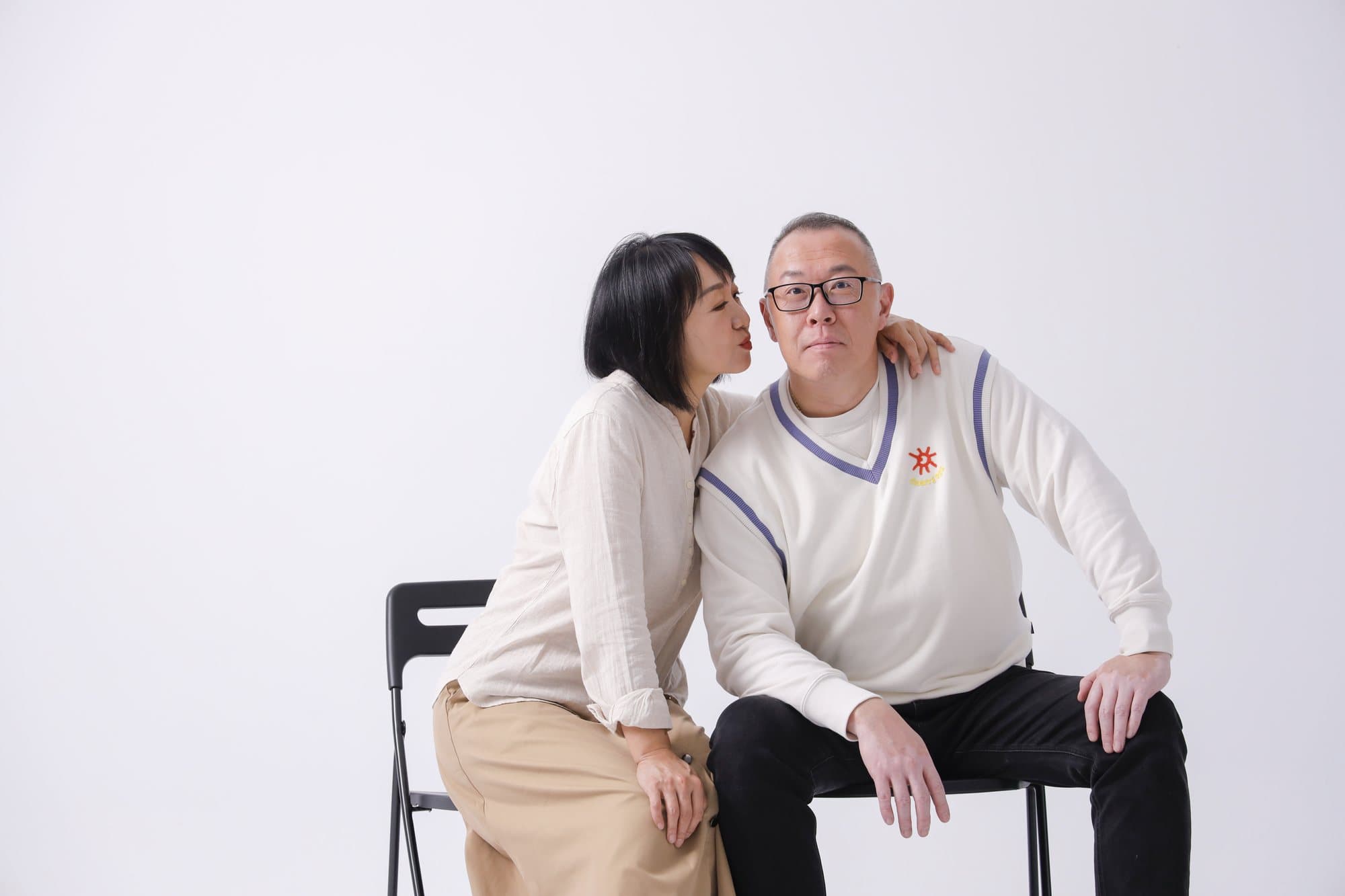 兩人並坐折疊椅、女子側身貼近的白棚雙人像