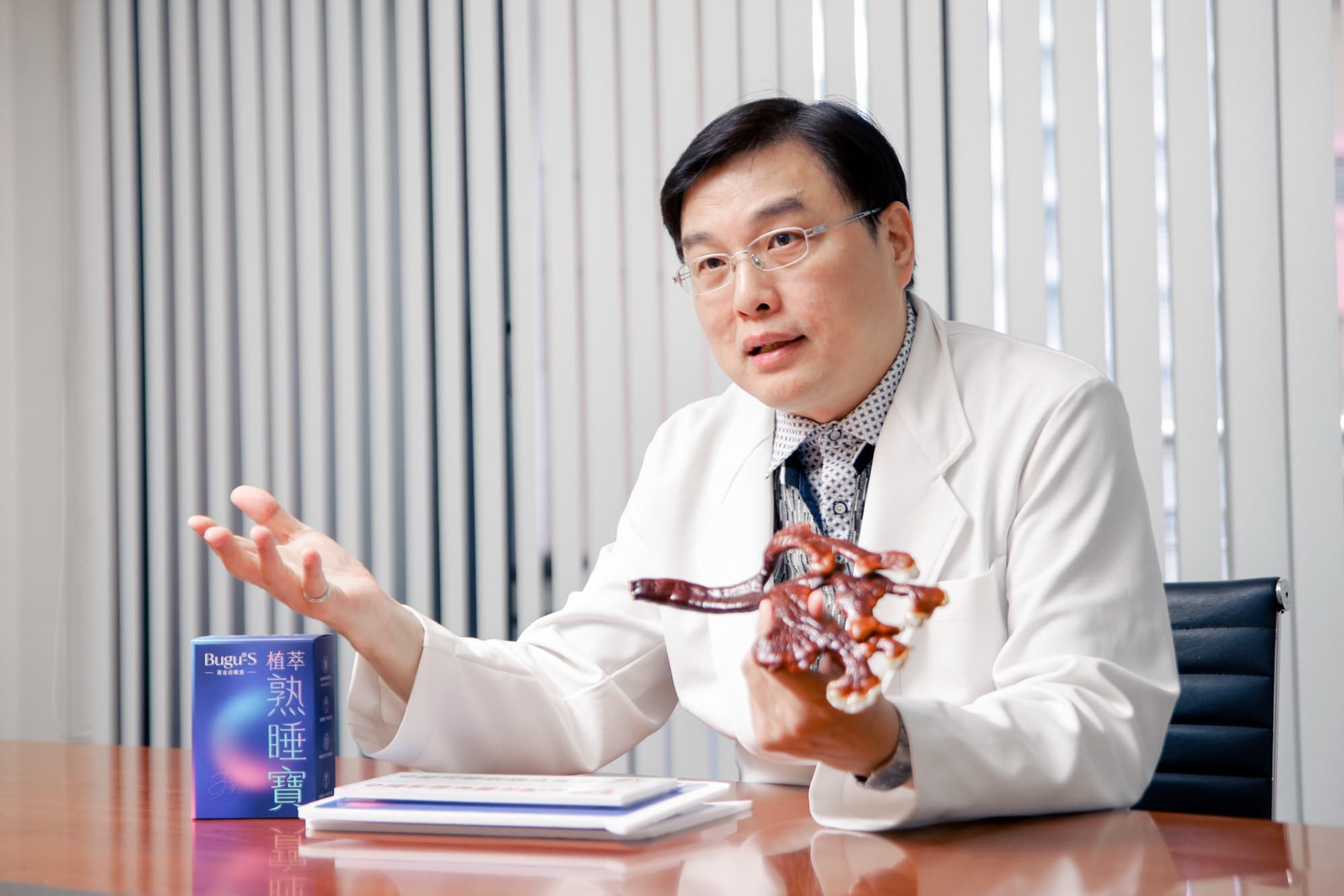 醫師受訪時手持鹿角靈芝標本邊講解的桌邊側拍