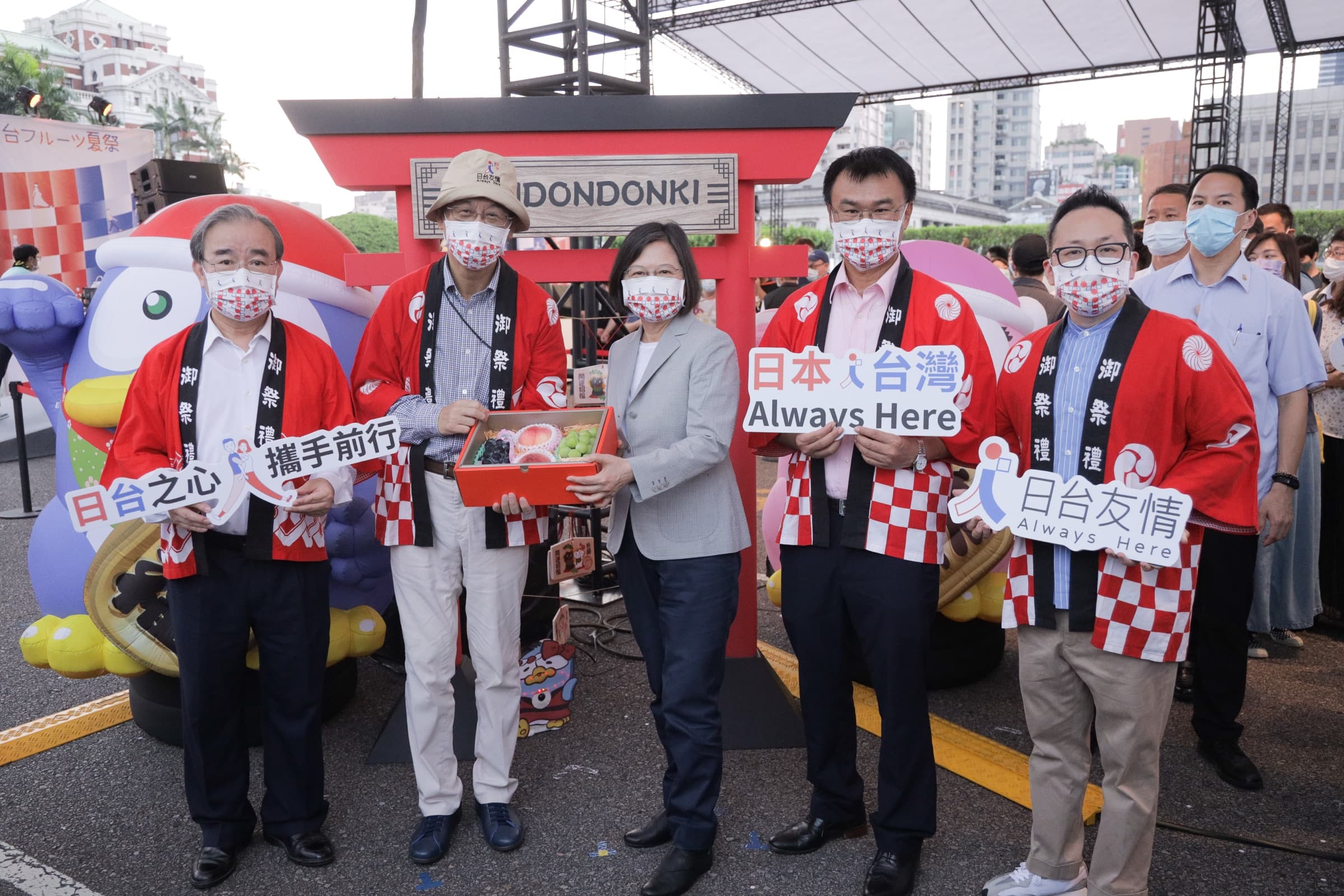 蔡英文總統居中,兩側身著紅色『御祭禮』法被的與會者手持『日台之心 攜手前行』『日本×台灣 Always Here』『日台友情』識別牌,於紅色鳥居造型攤位前合影