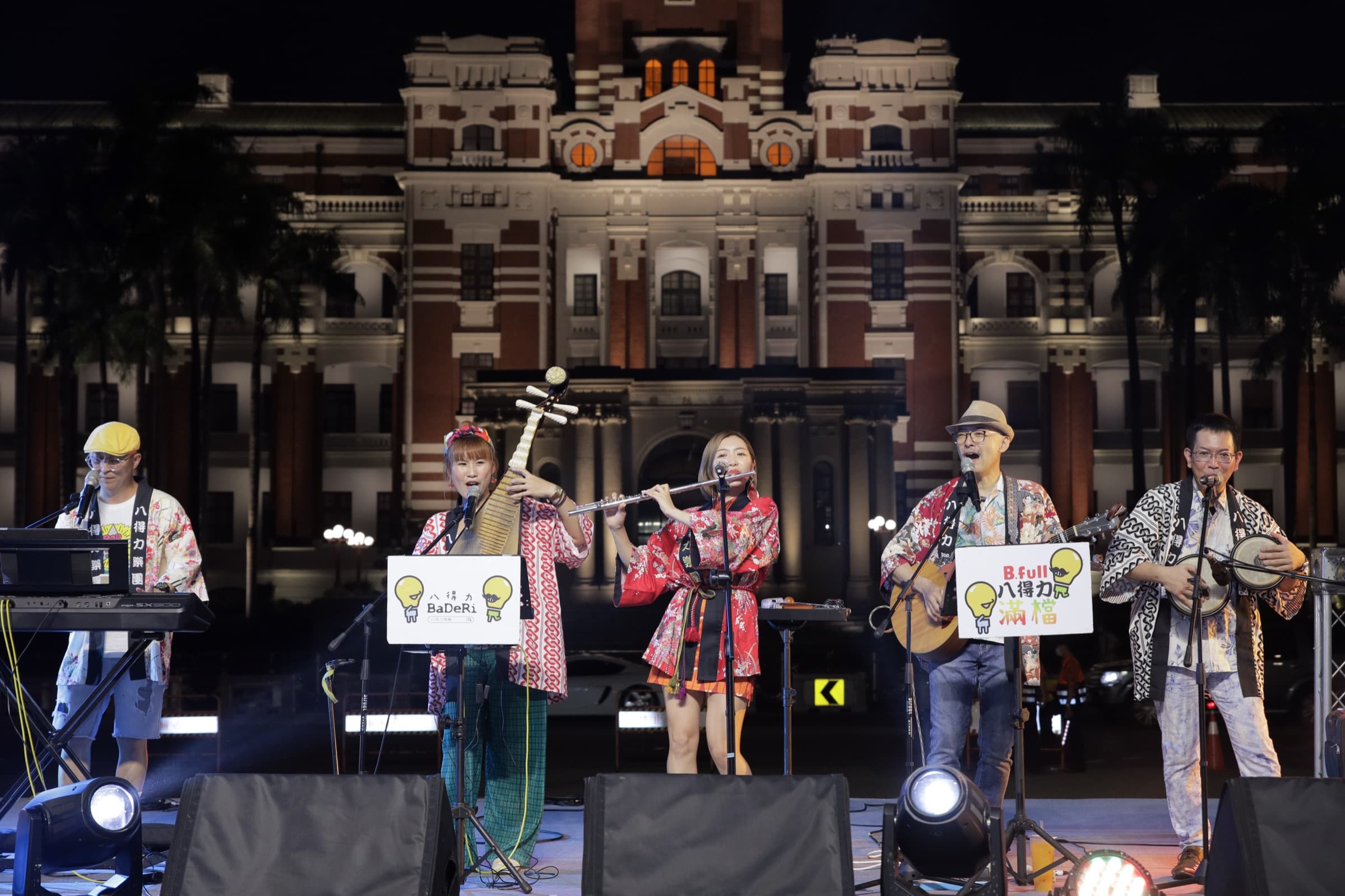 五人樂團身著和風法被與服飾,在夜間打光的總統府前舞台上演奏琵琶、長笛、吉他與打擊樂器