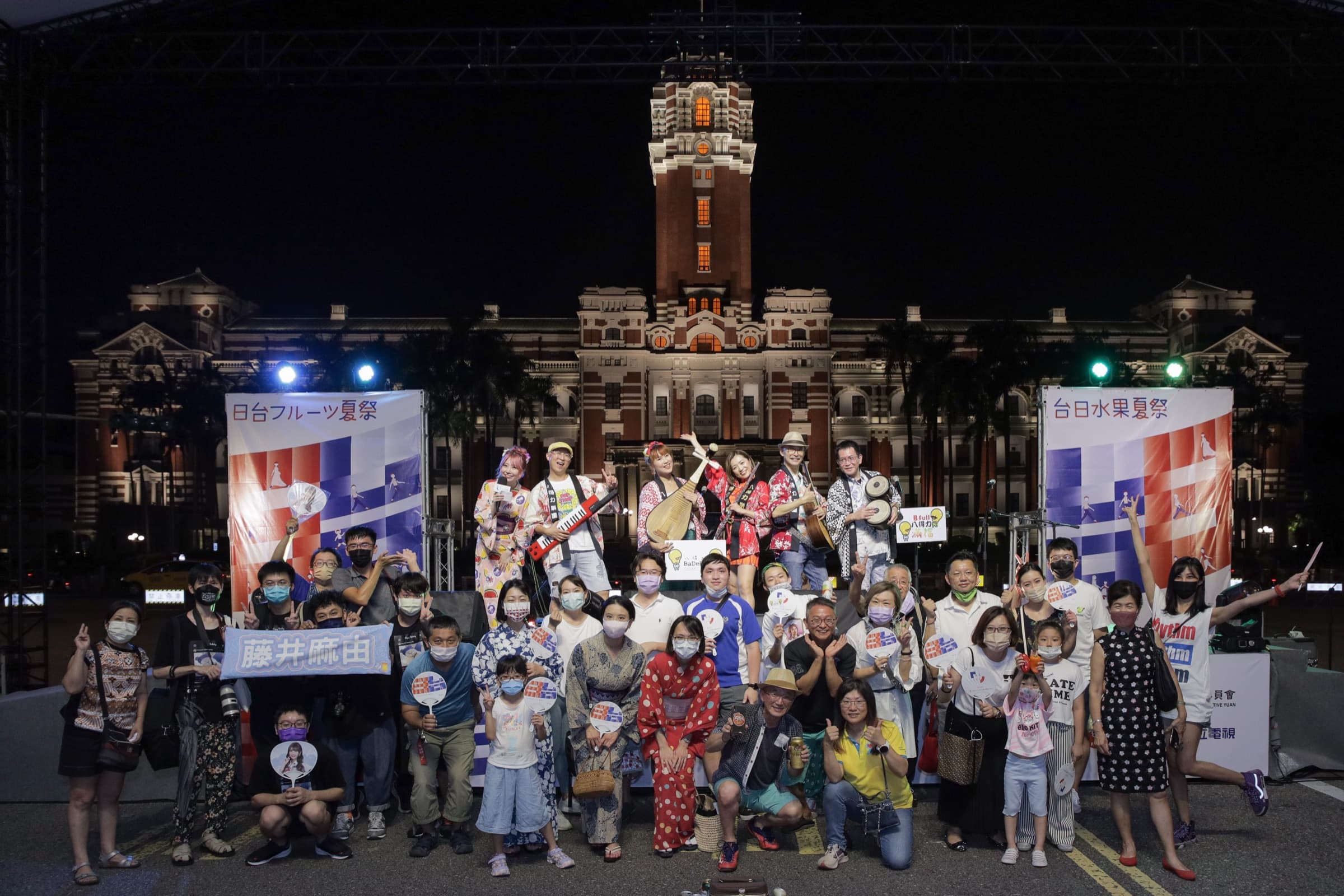 夜間打光的總統府前,演出樂團與眾多手持團扇的現場觀眾一同入鏡的大合照
