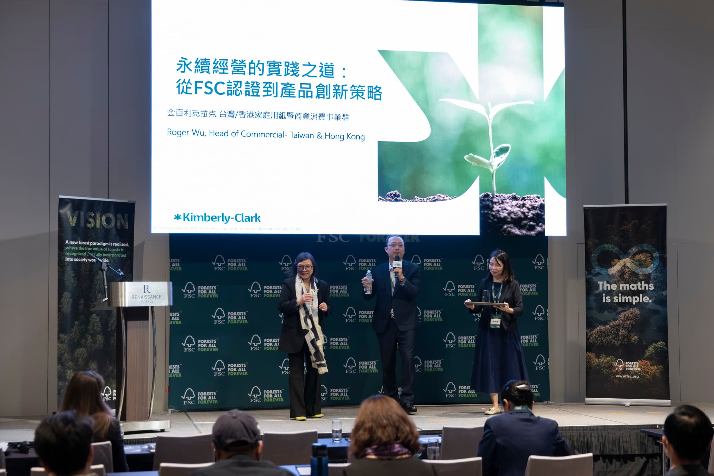 三位講者並排站在舞台上分享,身後大螢幕顯示簡報標題與企業品牌標誌