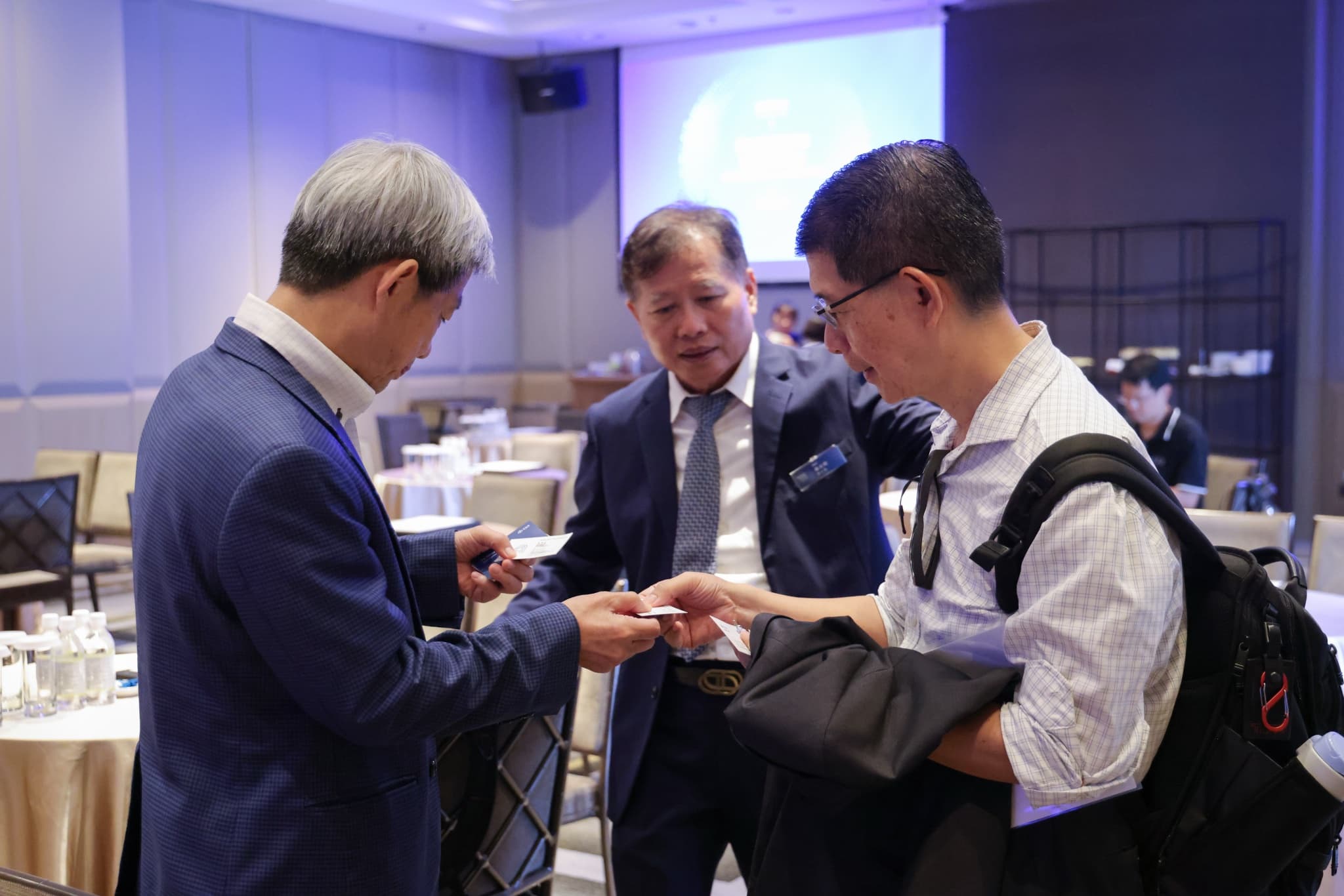 三位與會者在會場圓桌旁交換名片交談