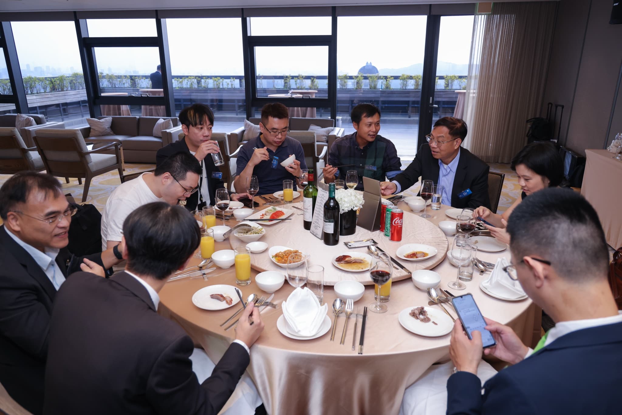 高樓層宴會廳圓桌晚宴,與會者邊用餐邊交談,落地窗外是城市景觀