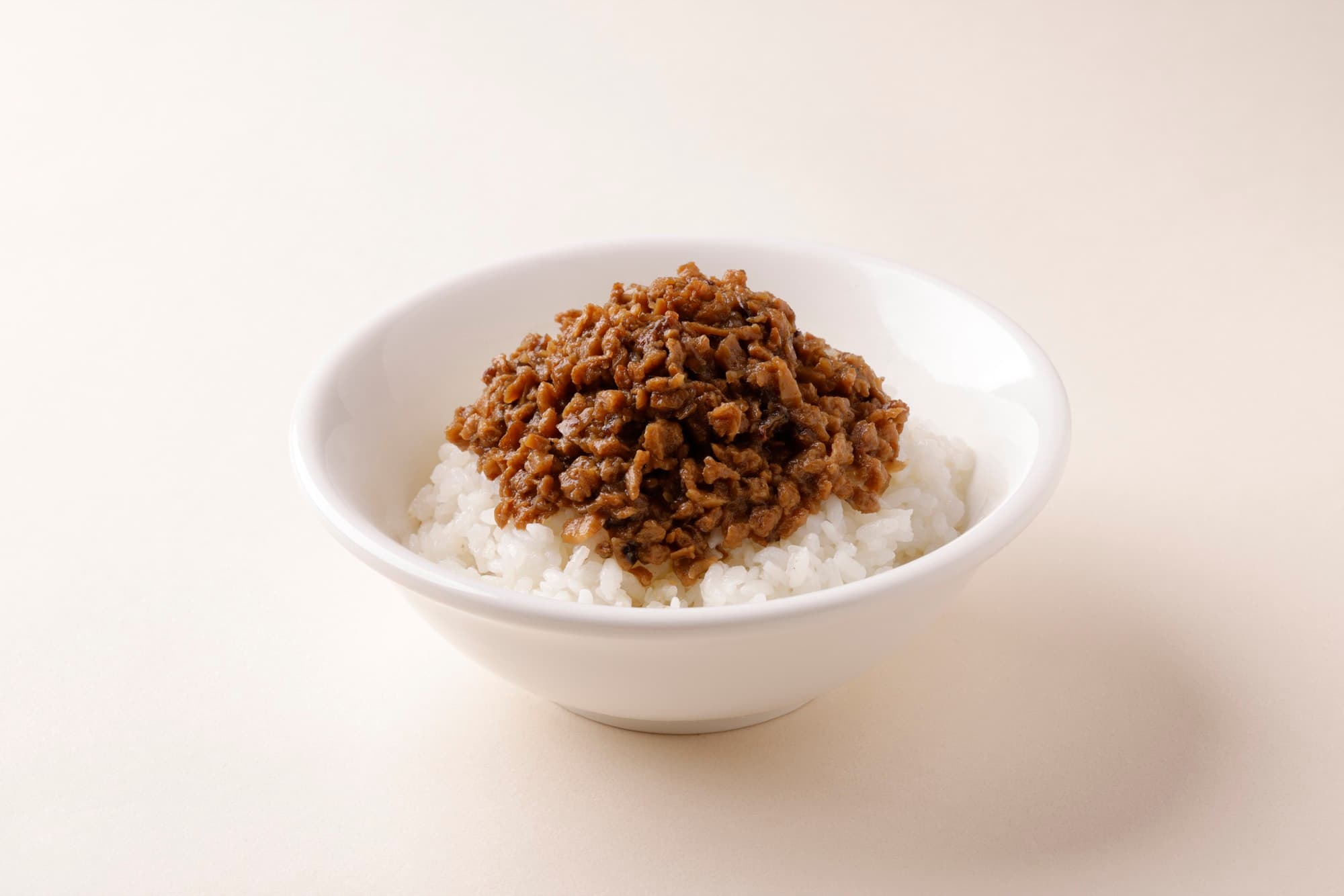 白瓷碗白飯上盛一團醬色肉燥,乾淨米色背景