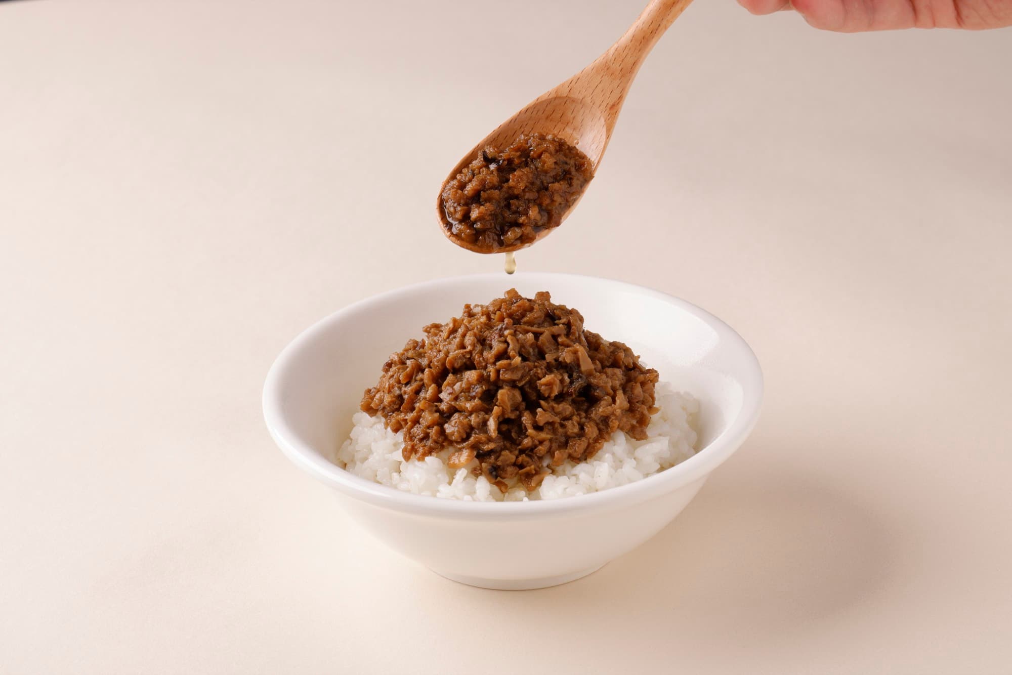 木匙舀起肉燥懸在飯碗上方,一滴醬汁滴落