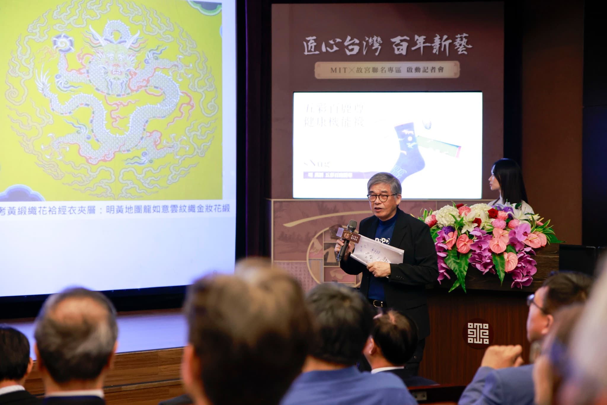 品牌代表在「匠心台灣 百年新藝」背板與明黃龍紋織品投影前,手持資料介紹五彩百鹿尊聯名襪