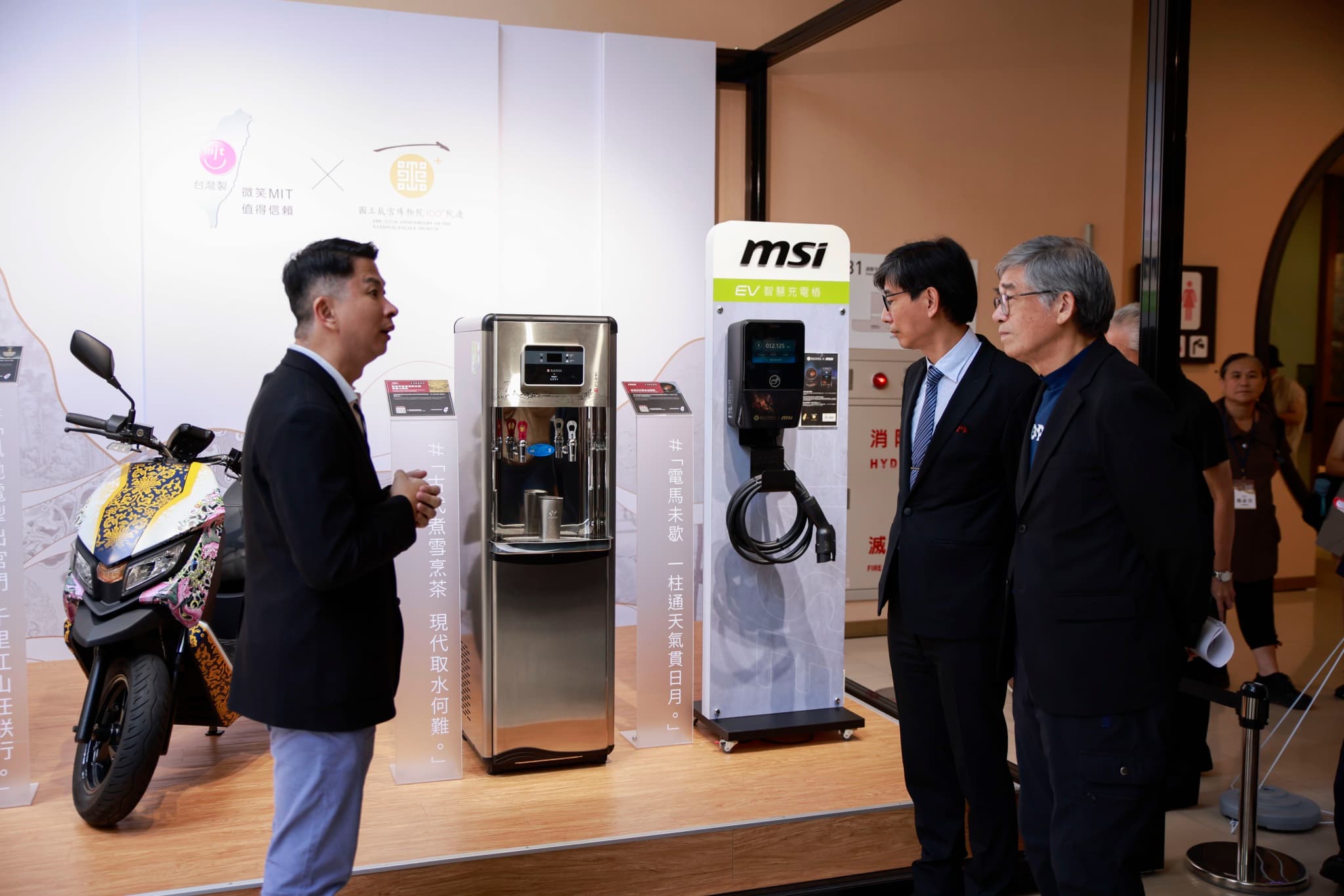 展售區陳列彩繪電動機車、不鏽鋼飲水機與MSI EV充電樁,牆面印有台灣MIT與故宮聯名標誌,貴賓聽取導覽