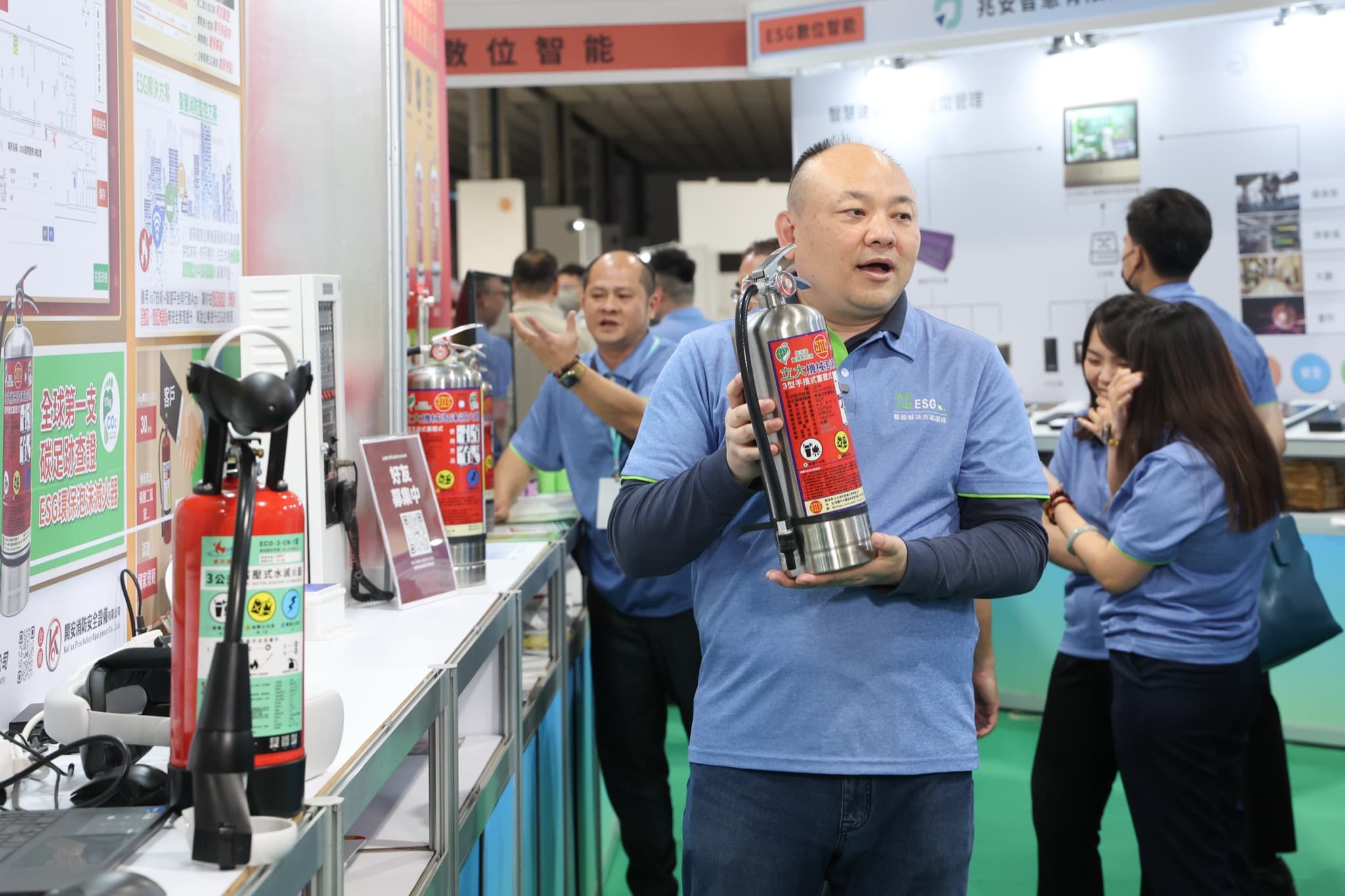 平安消防人員手持不鏽鋼滅火器向參觀者解說,展台陳列紅色與不鏽鋼多款滅火器