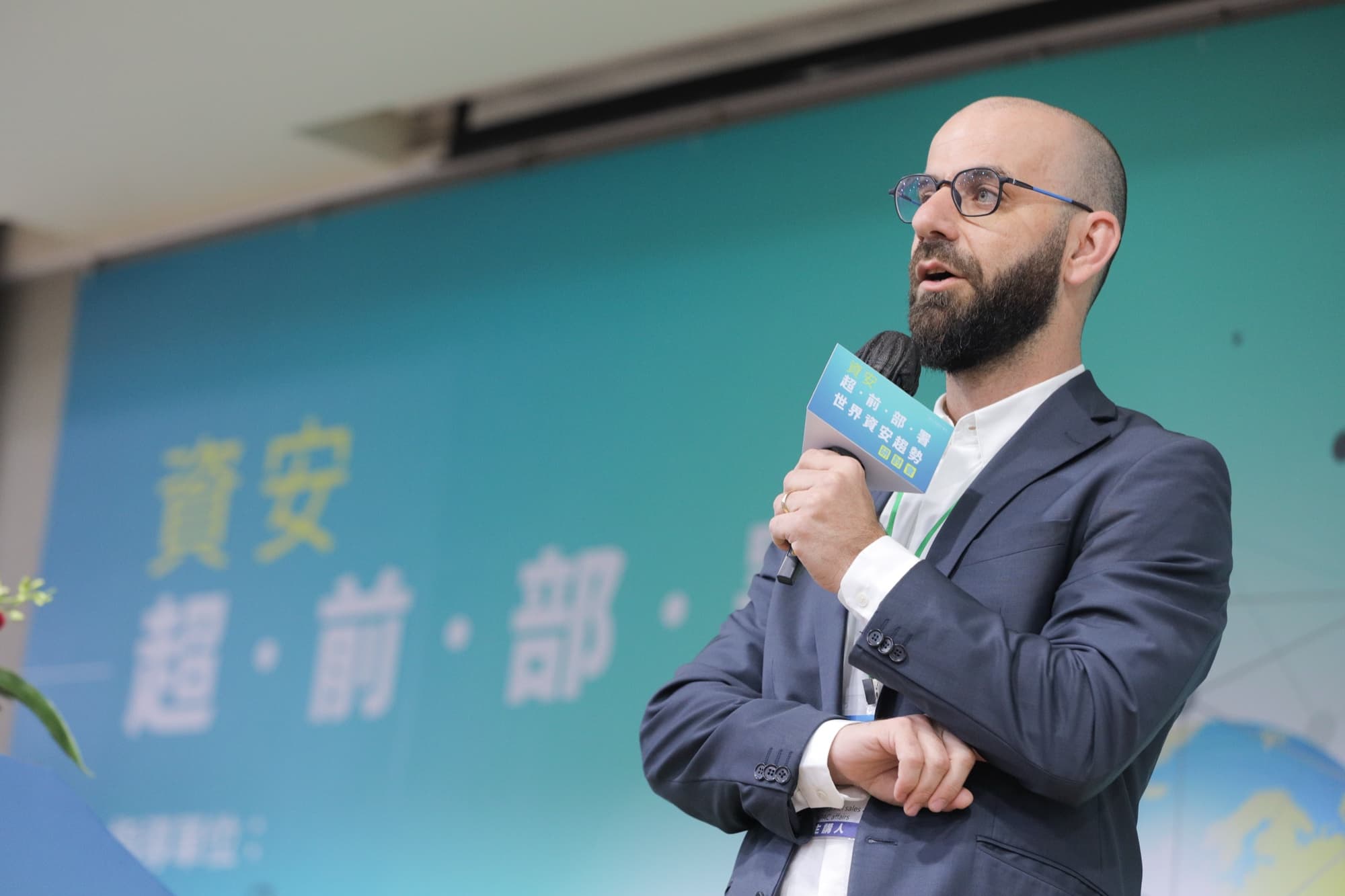 外國講者於背板前持麥演講