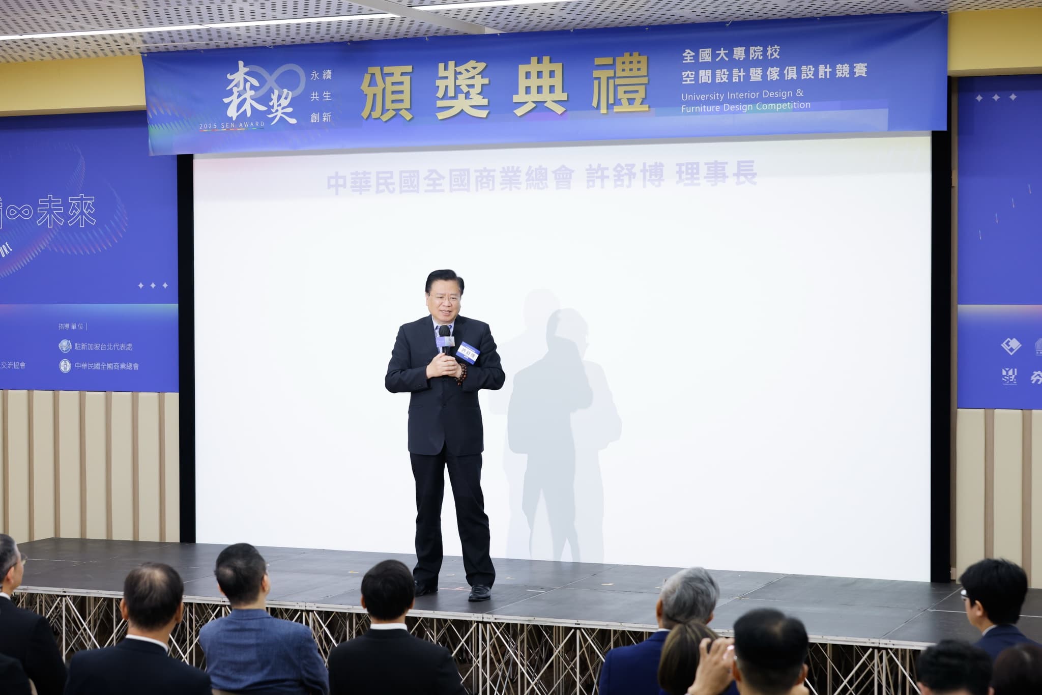 貴賓站在舞台投影幕前致詞,幕上字幕為中華民國全國商業總會許舒博理事長