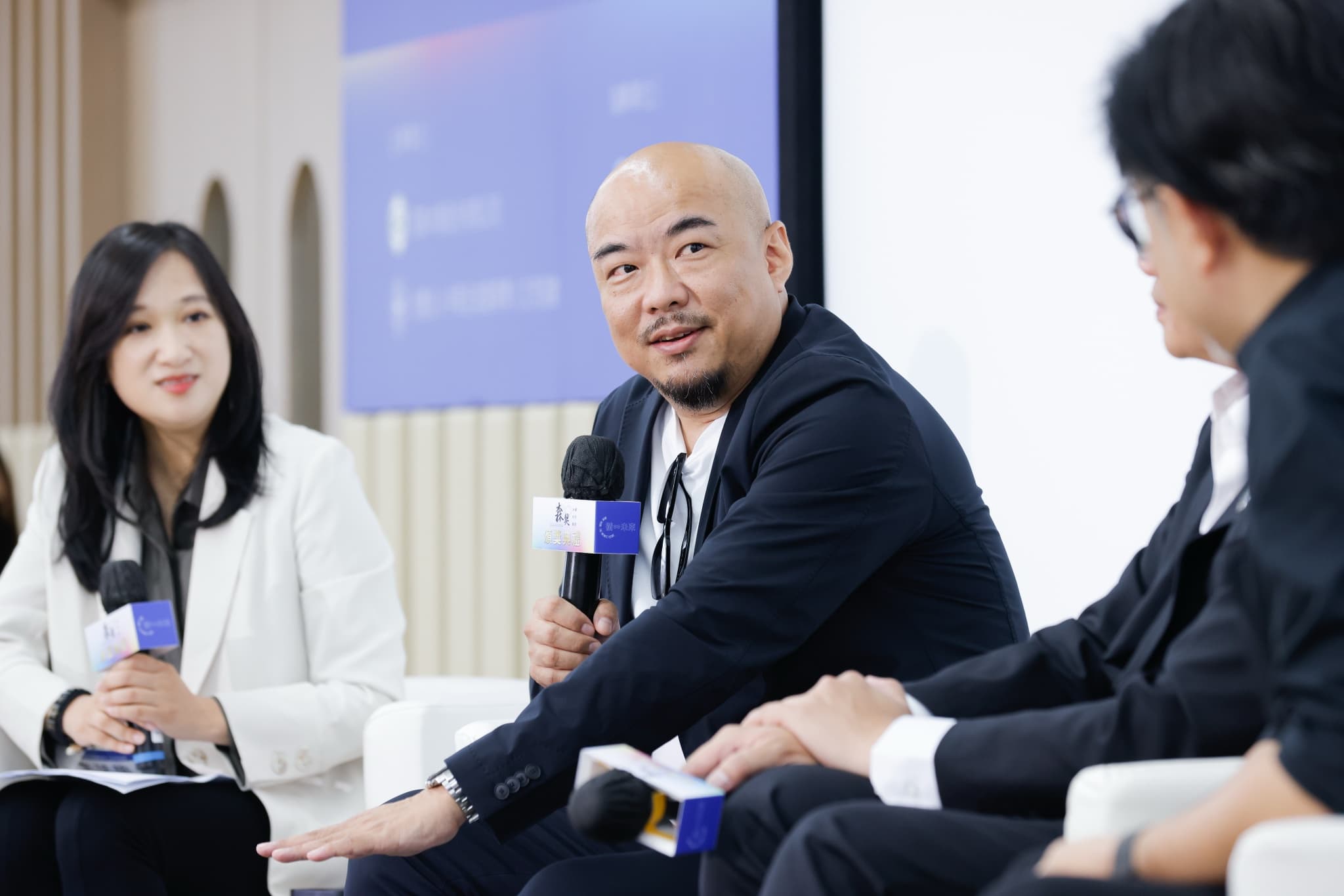 座談論壇中講者手持麥克風發言,左右兩側與談人聆聽