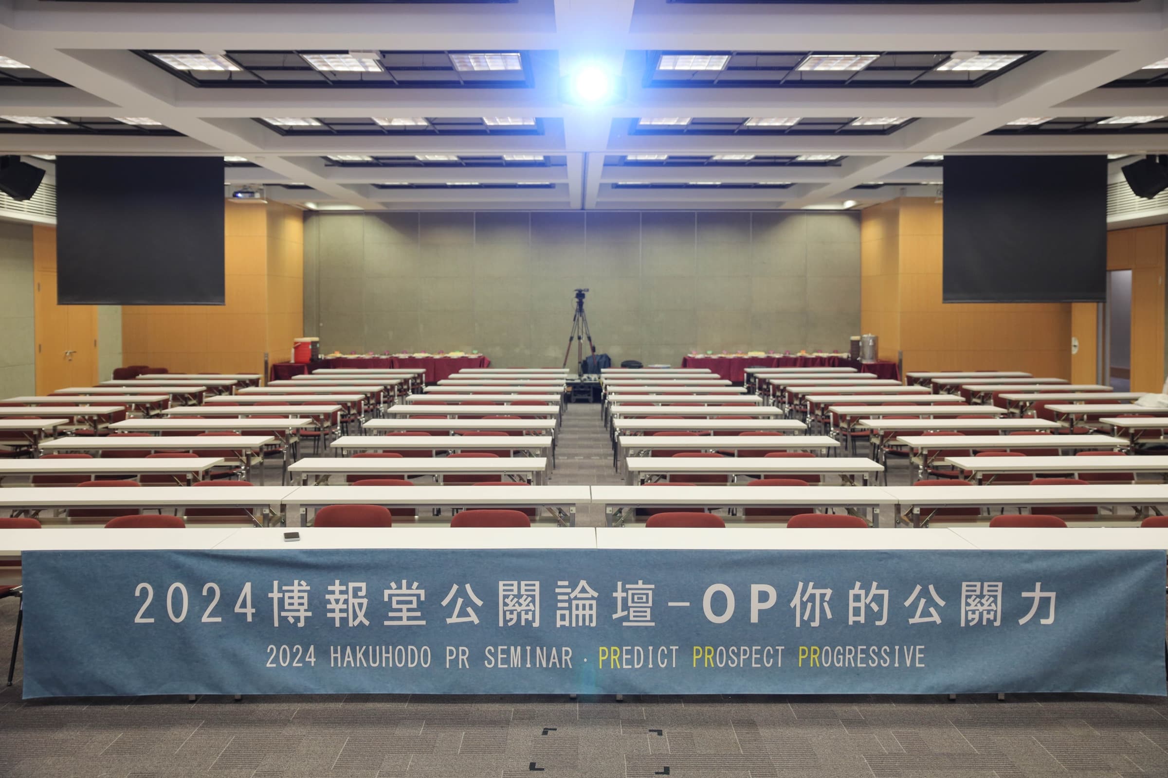 開場前的講廳,舞台前方橫幅寫著『2024 博報堂公關論壇 HAKUHODO PR SEMINAR OP 你的公關力』,整齊排列的座位區