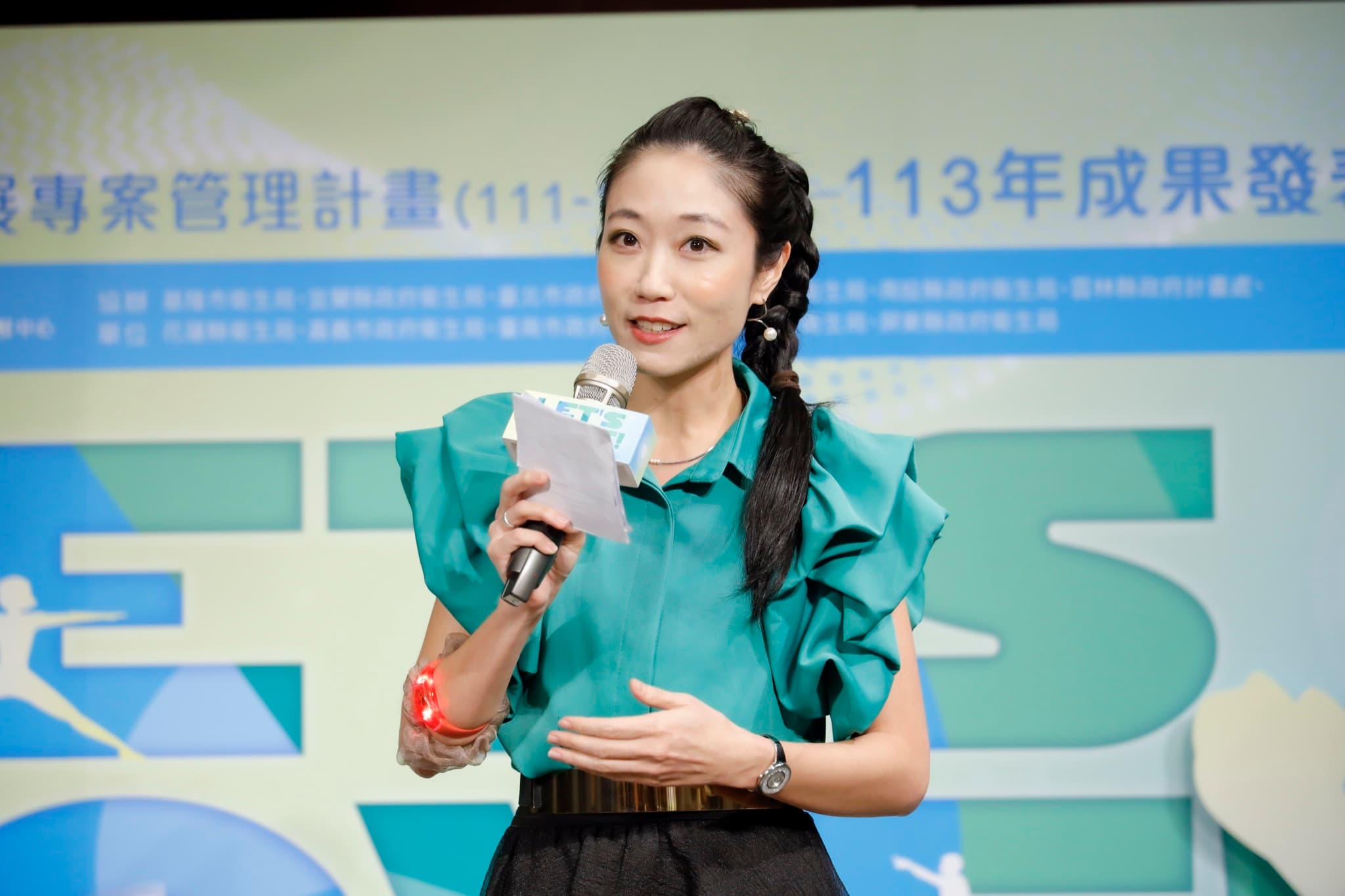 主持人持稿與麥克風開場,背板上方可見「113年成果發表會」字樣與協辦衛生局名單