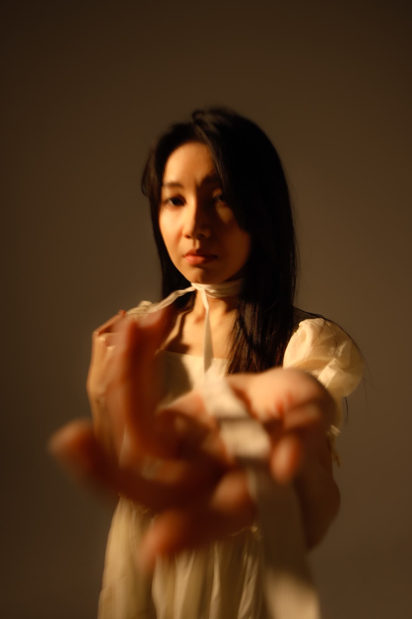 女子向鏡頭伸出雙手、臉部柔焦的半身像,暖調棚燈