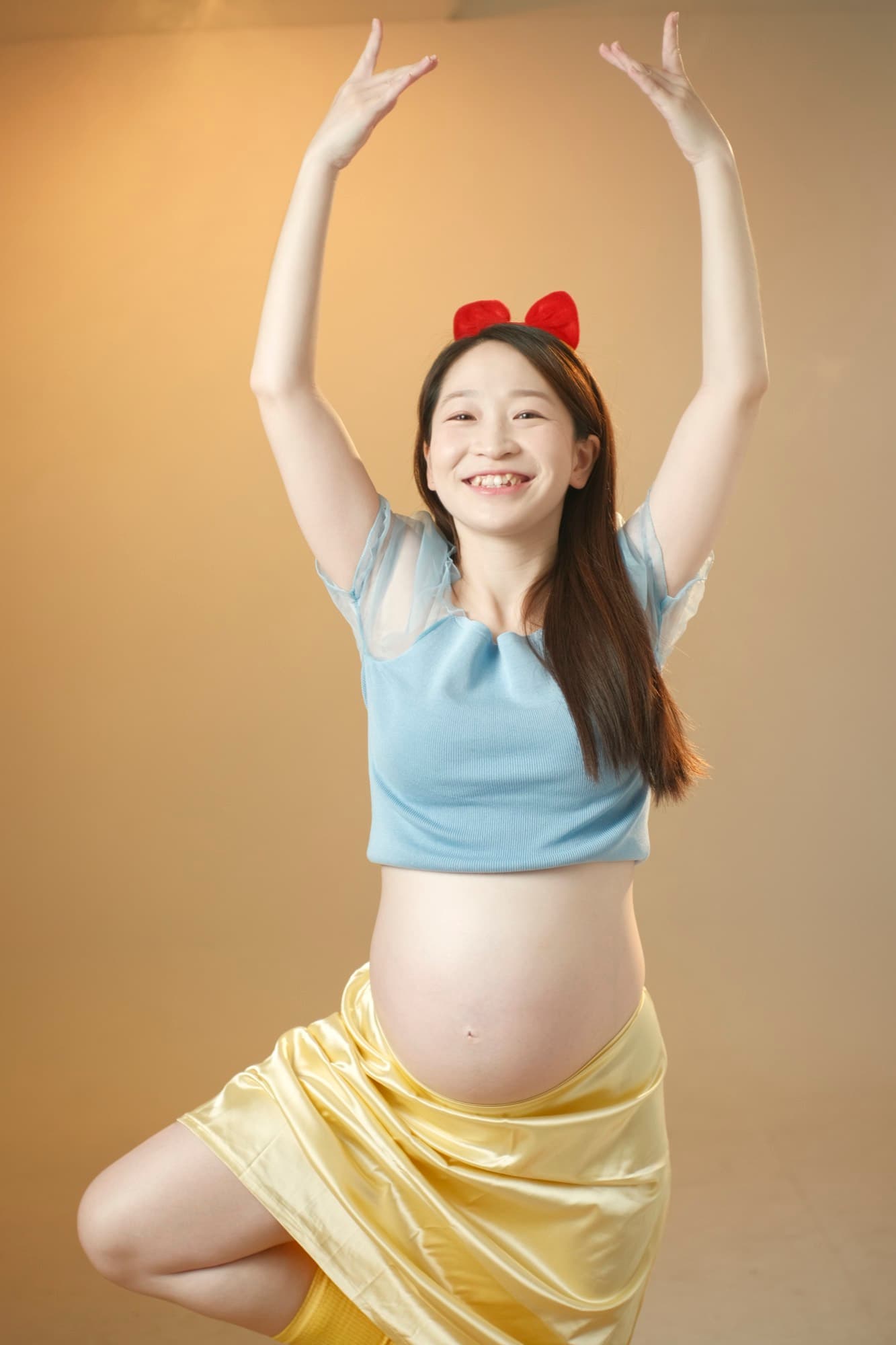 孕婦雙臂高舉、燦笑的全身動感人像,暖橘背景