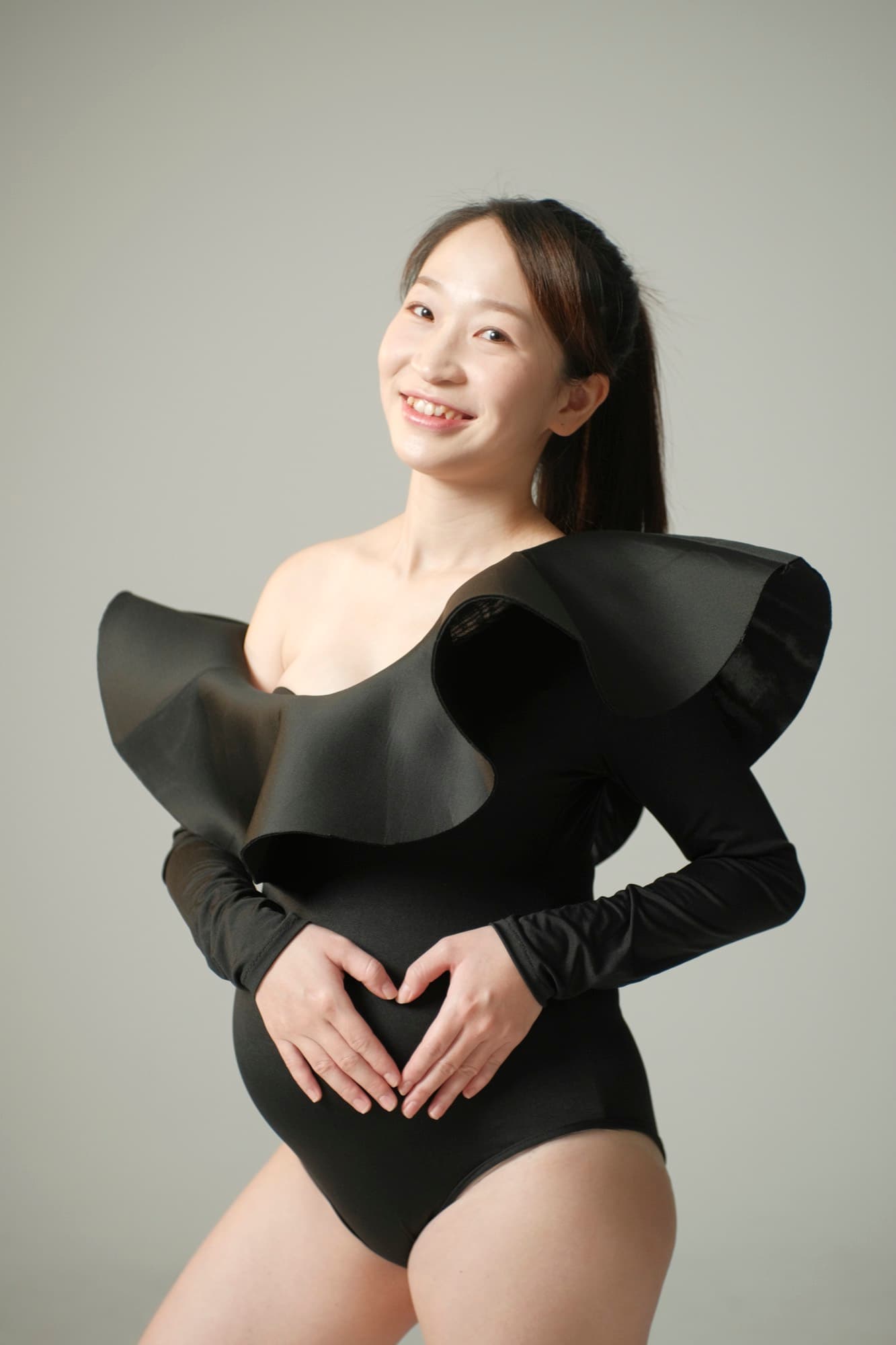 黑色荷葉領連身衣孕婦以雙手在腹前比心