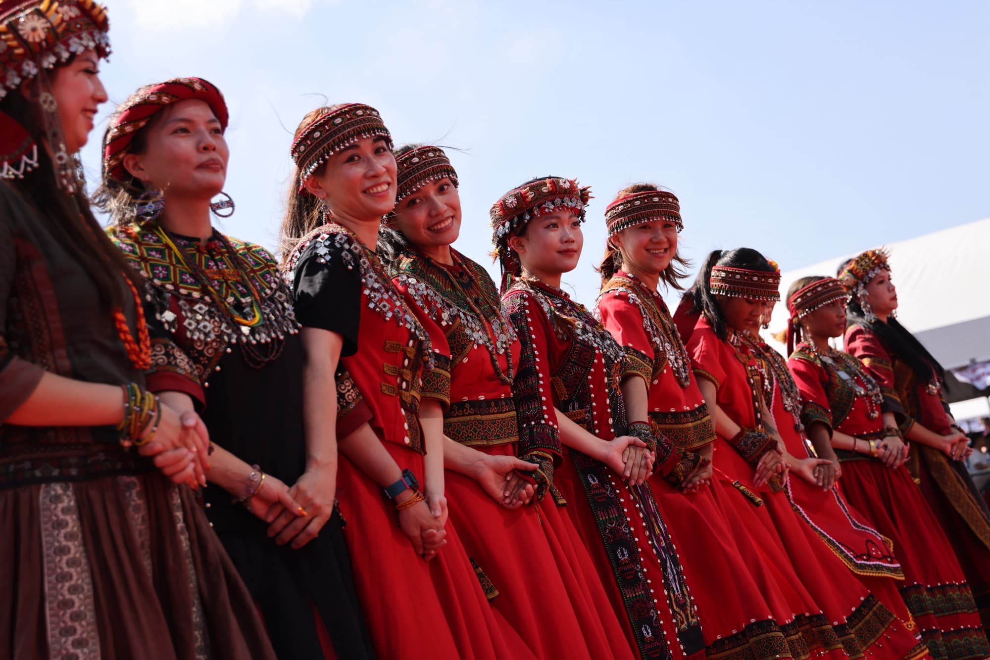 一排紅色族服女性牽手並列,天空為背景