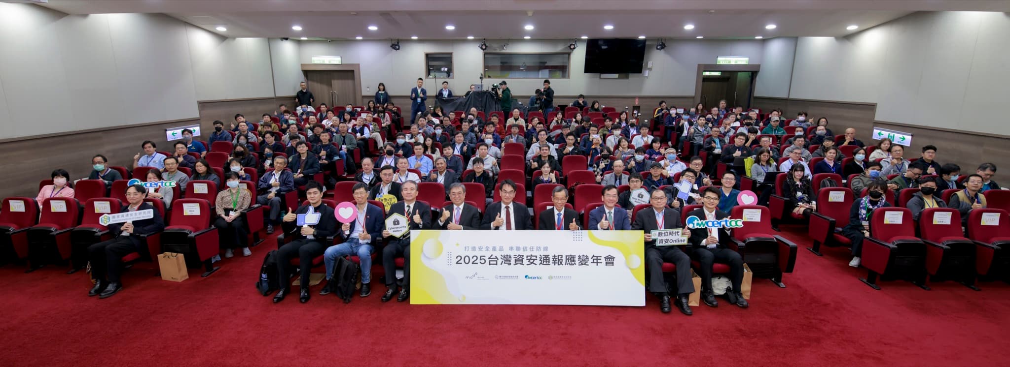 禮堂全景大合照,百餘位與會者比讚,前排貴賓持年會主視覺板與TWCERT/CC手板