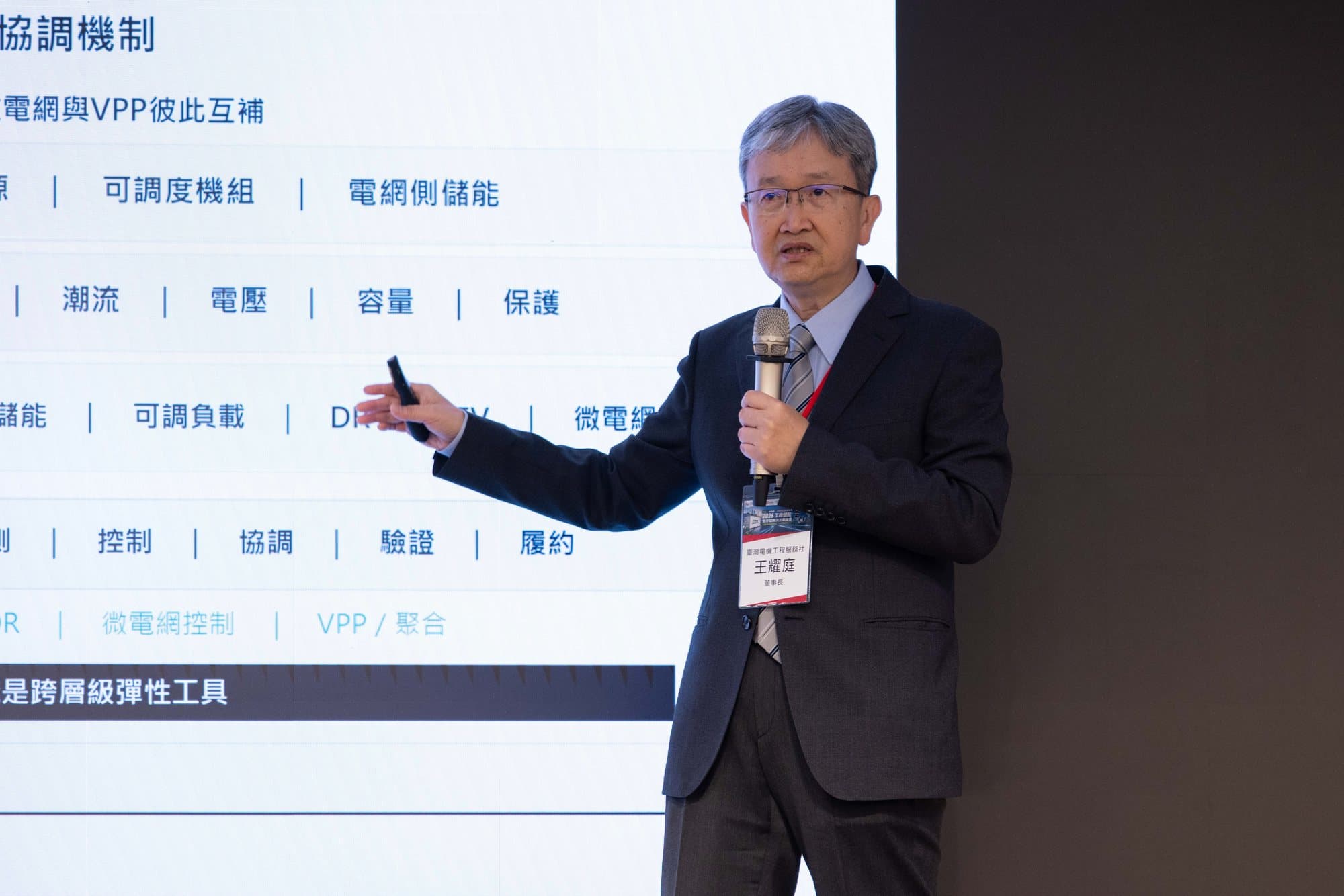 講者手持麥克風,側身指向身後的簡報畫面說明內容