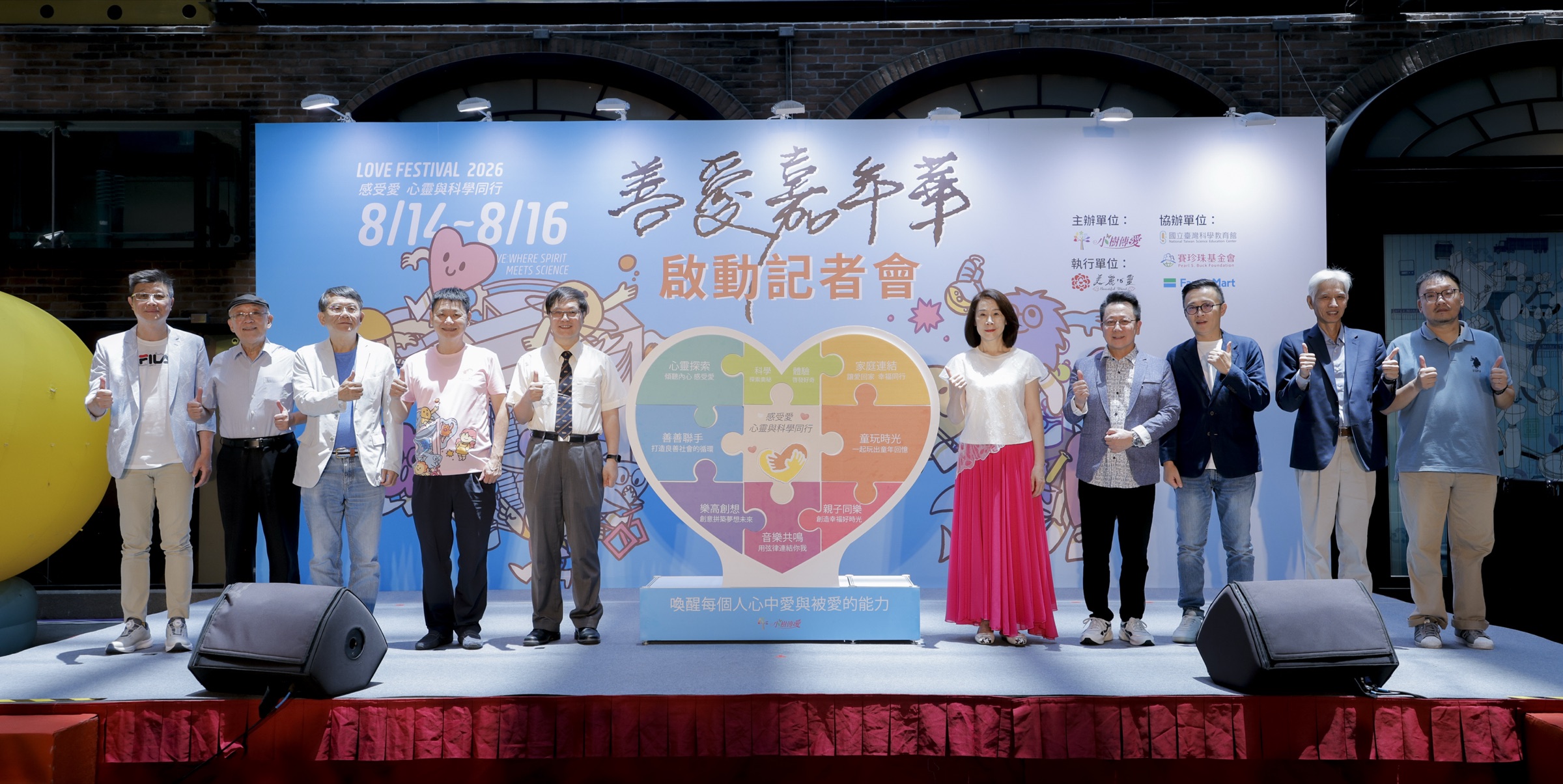 2026 善愛嘉年華啟動記者會，十位與會貴賓於活動主視覺與「八大主題」愛心拼圖前合影